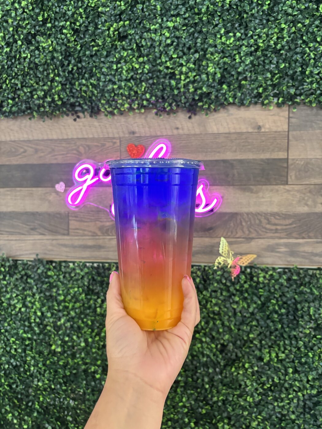 Layered rainbow energy tea against the green hedge wall and pink neon at Casa Grande Nutrition